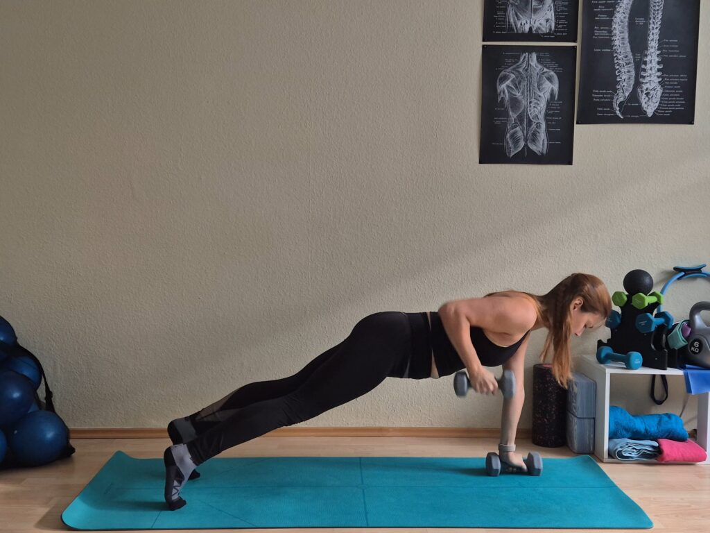 Person performing a side-bodyweight exercise on a blue mat in a home gym, with dumbbells and various weights nearby and exercise posters on the wall.